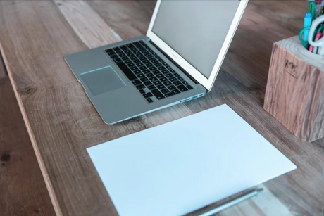 A laptop and pen on a wooden table, suggesting a workspace setup, reflecting 'Brute Status' focus on customized, optimized accessories.