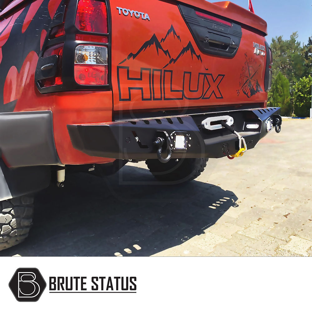 Toyota Hilux 2015+ rear bumper in matt black, featuring knock-out holes for sensors and integrated lights, displayed on the back of a red truck.