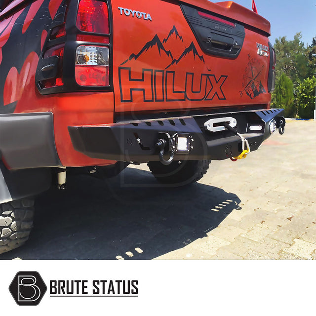 Toyota Hilux 2015+ rear bumper in matt black, featuring knock-out holes for sensors and integrated lights, displayed on the back of a red truck.