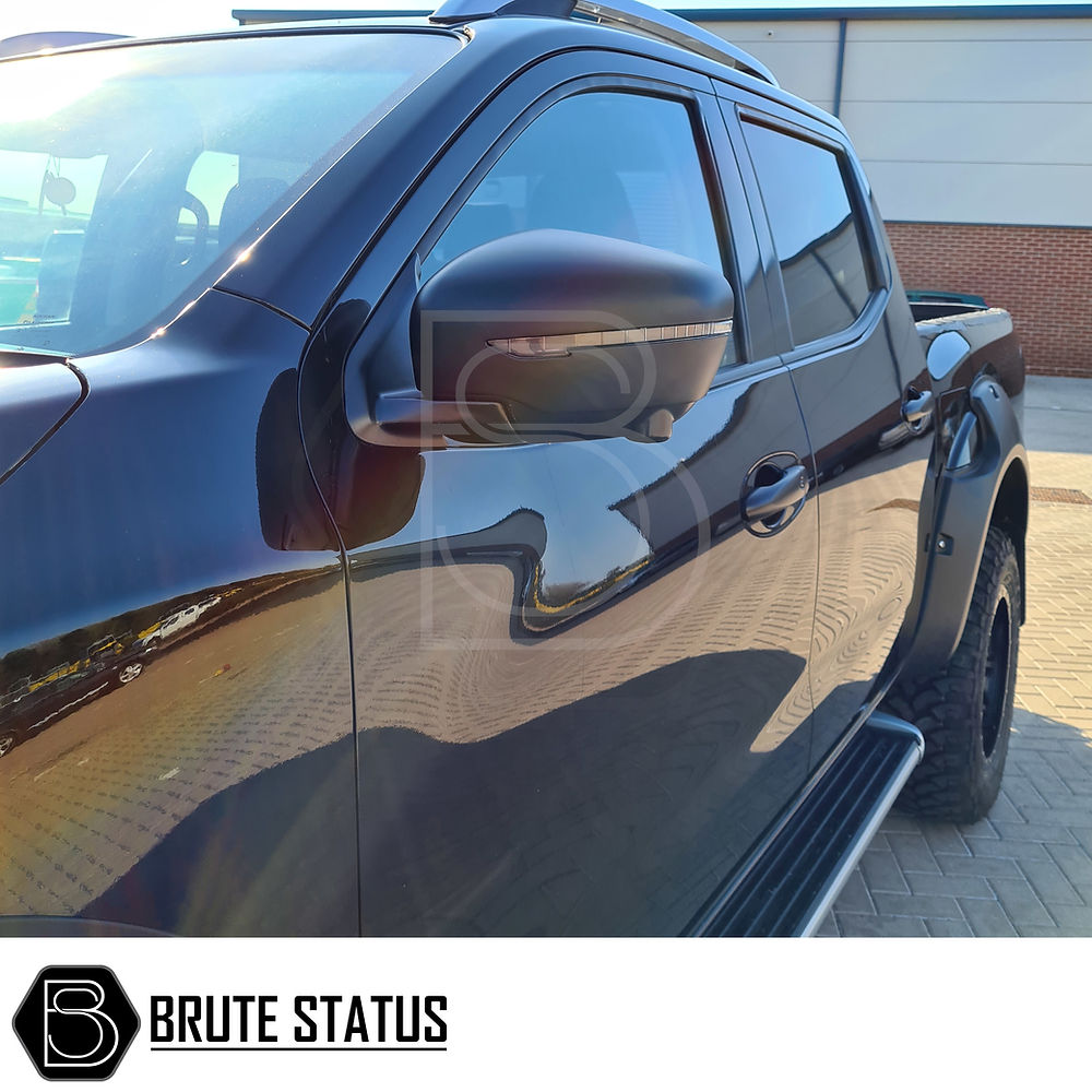 Nissan Navara NP300 2015-2022 Wing Mirror Covers (Matt Black) displayed on a black truck in a parking lot, highlighting their sleek, easy-to-install design.